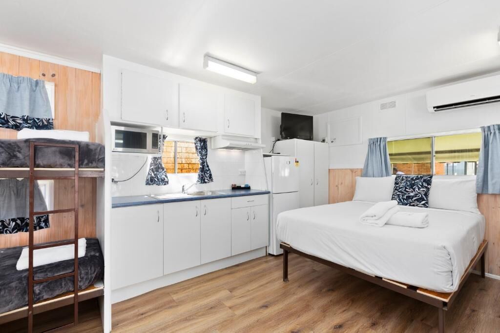 A compact room with a bunk bed, kitchenette, and a single bed.