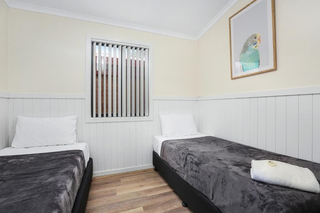 Una habitación con dos camas, una ventana con persianas, un cuadro en la pared y una toalla blanca sobre una cama.