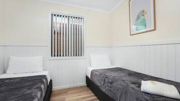 Una habitación con dos camas, una ventana con persianas, un cuadro en la pared y una toalla blanca sobre una cama.