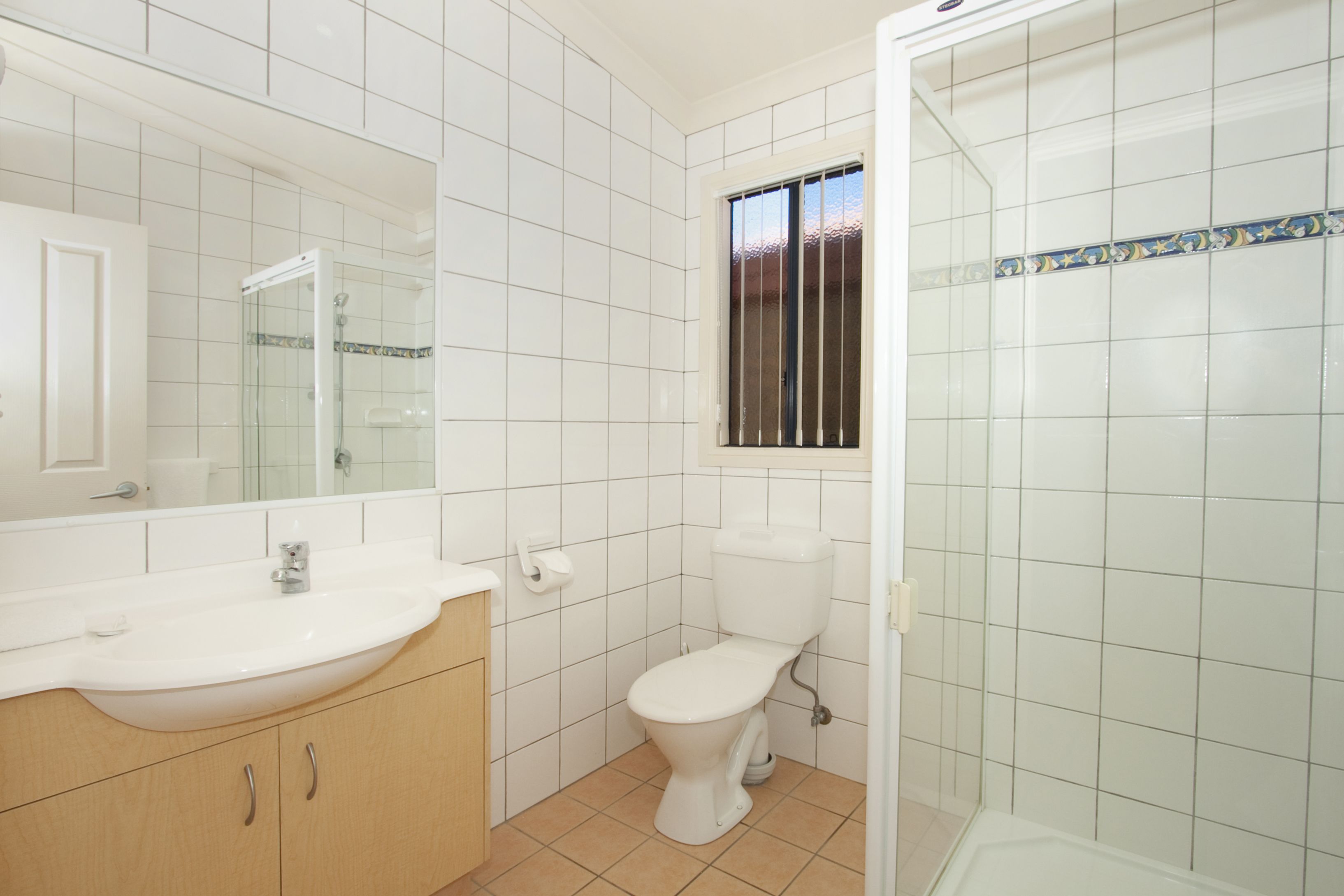 A bathroom with white tiles, a sink, a toilet, and a shower.