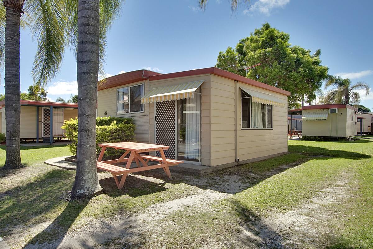 A single-story mobile home with a picnic table in front, surrounded by grass and palm trees.