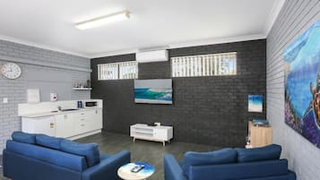 Ein modernes Wohnzimmer mit Küchenbereich, ausgestattet mit einer Sofagarnitur, einem Flachbildfernseher und Kunstwerken an den Wänden.