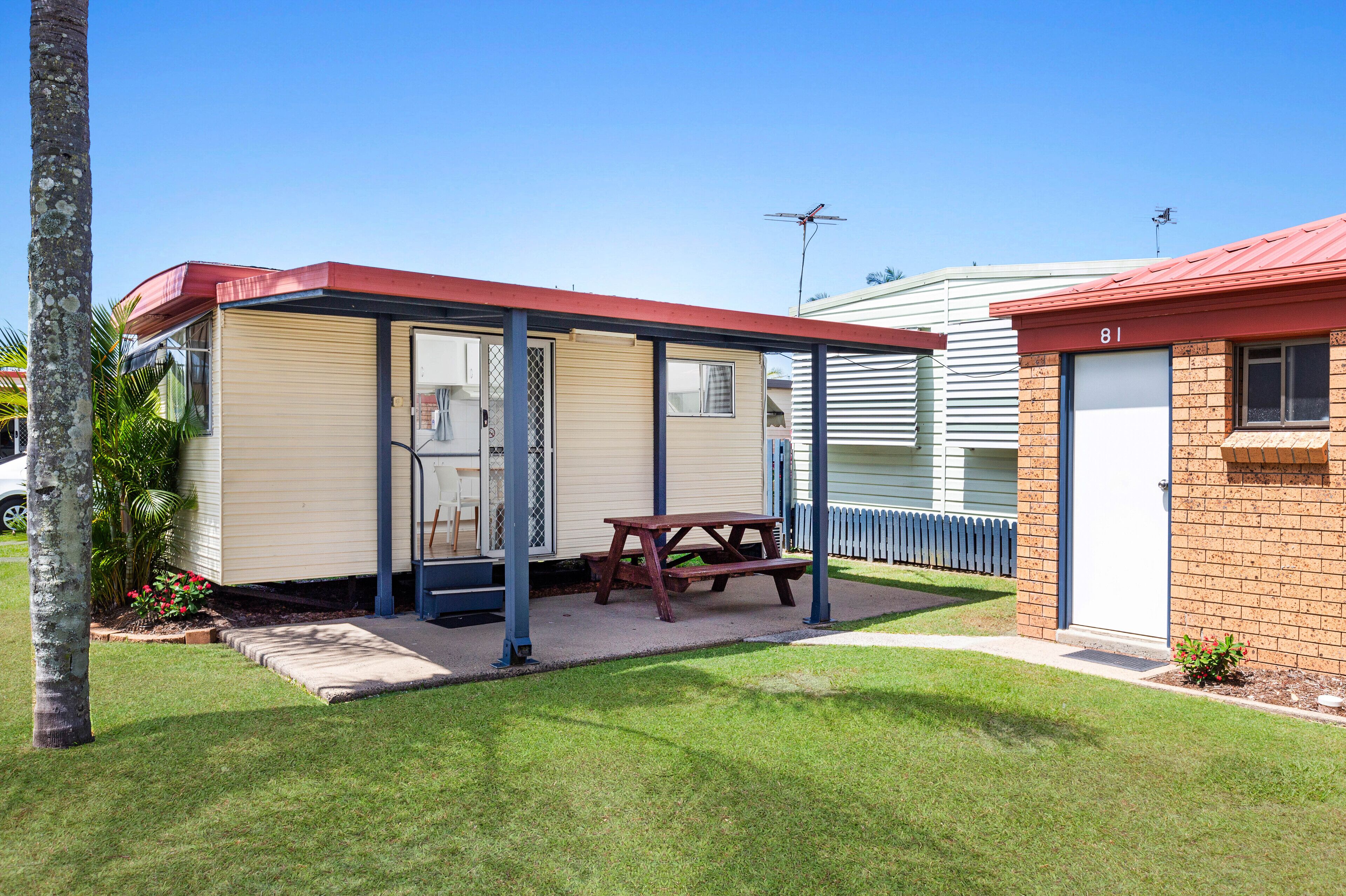 A mobile home with a covered patio, a picnic table, and a small garden area.