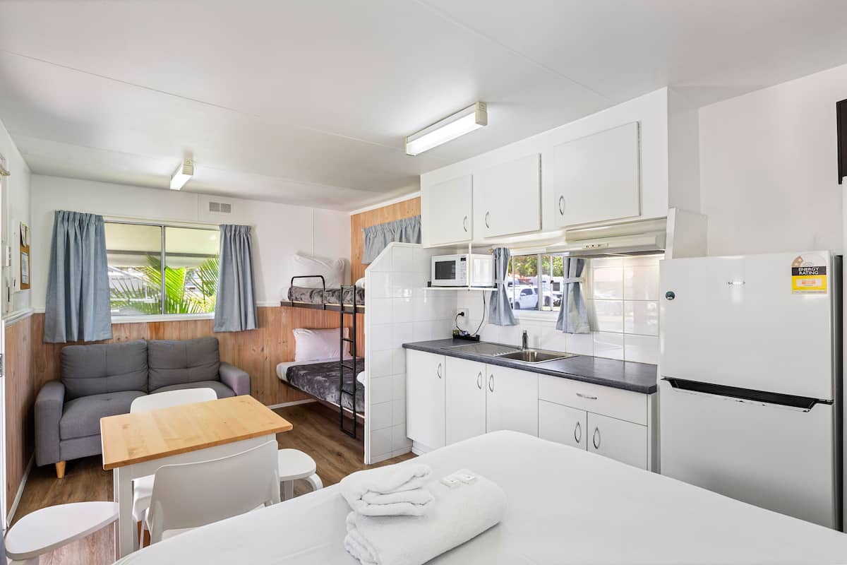 A compact, well-lit room with a kitchenette, a sofa, a small dining table, and a bed.