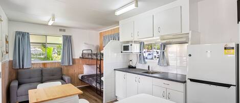 Habitación pequeña y luminosa con kitchenette, sofá, una pequeña mesa de comedor y una cama.