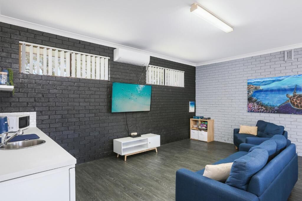 A modern living room with a dark brick wall, a flat-screen TV, a blue sofa, and a wooden cabinet.