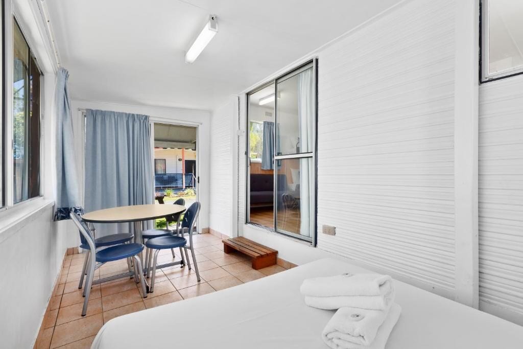 A hotel room with a bed, a table with chairs, a balcony, and a view of the outside.