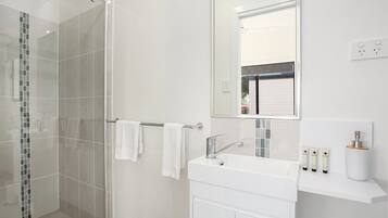 Un baño moderno con cabina de ducha de vidrio, un lavamanos blanco y un espejo encima.