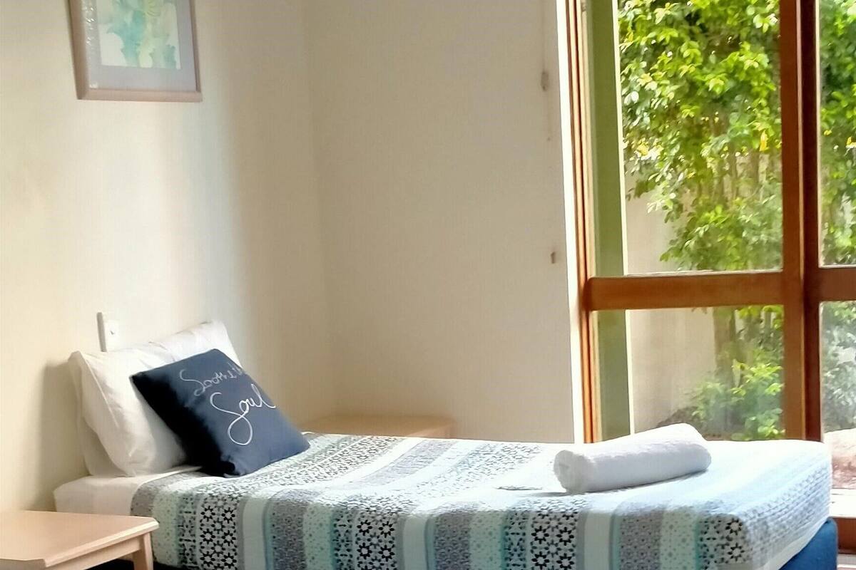Habitación de hotel con dos camas, una ventana con vistas a la vegetación y un cuadro en la pared.