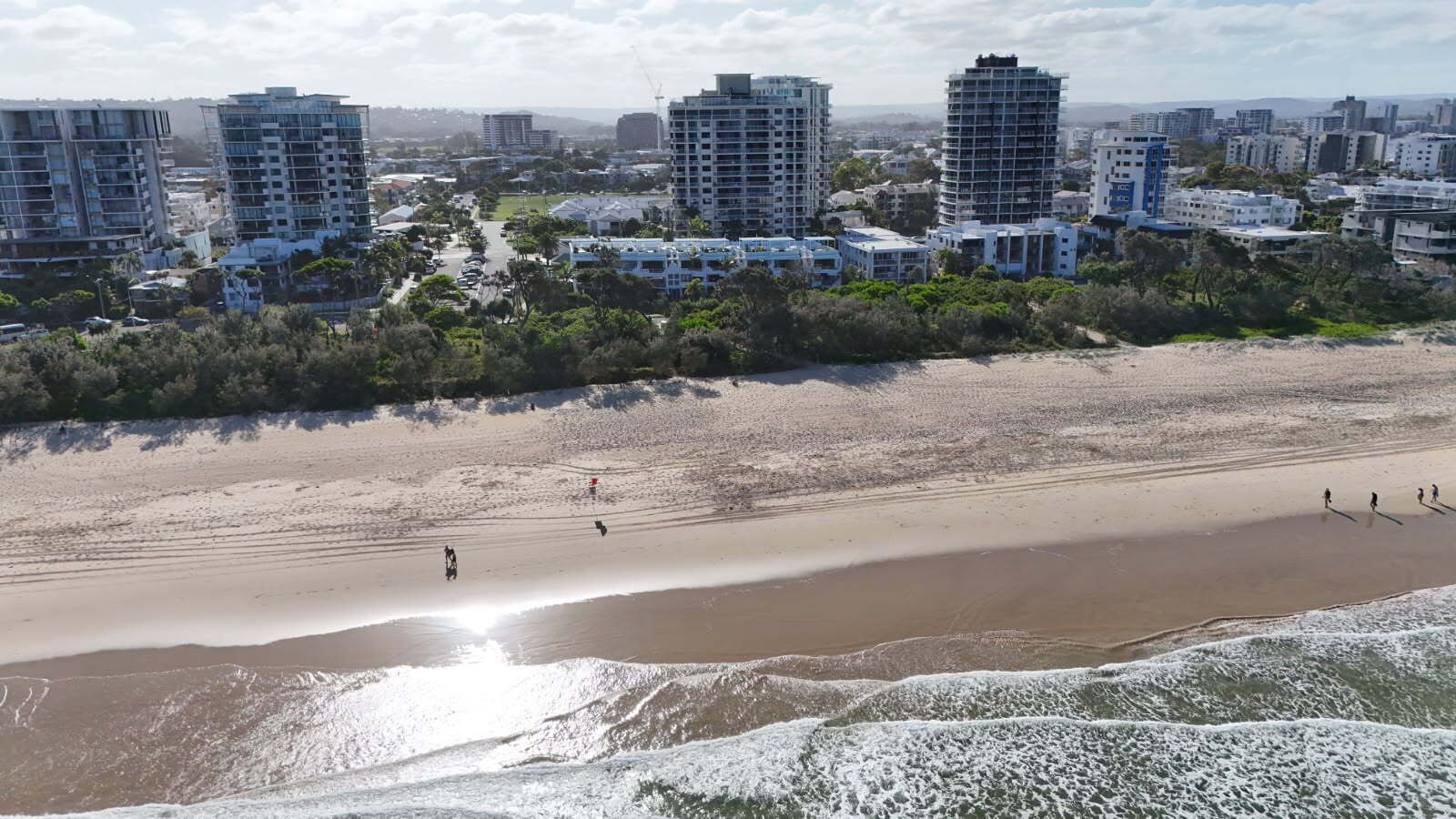 A coastal cityscape with high-rise buildings, a sandy beach, and a clear sky.