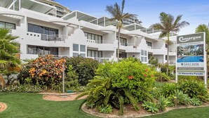 Un hotel moderno de varios pisos con balcones, rodeado de exuberante vegetación y palmeras.