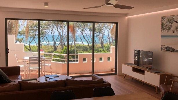 Una sala moderna con un amplio ventanal corredera que da a un balcón con vistas al mar.