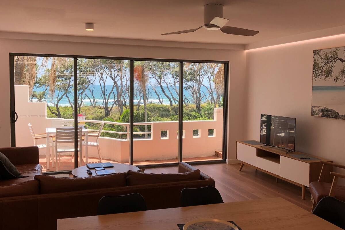 Una sala moderna con un amplio ventanal corredera que da a un balcón con vistas al mar.