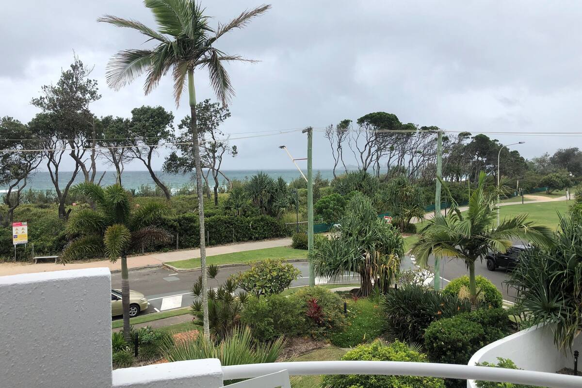 Un balcón con vistas al mar, rodeado de exuberante vegetación y palmeras.