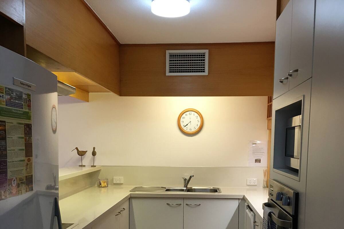Una cocina compacta con armarios blancos, un refrigerador de acero inoxidable, un microondas y un lavamanos.