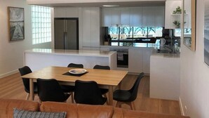 Una cocina moderna con una isla central, un comedor con mesa de madera y sillas negras, y un amplio ventanal que proporciona luz natural.
