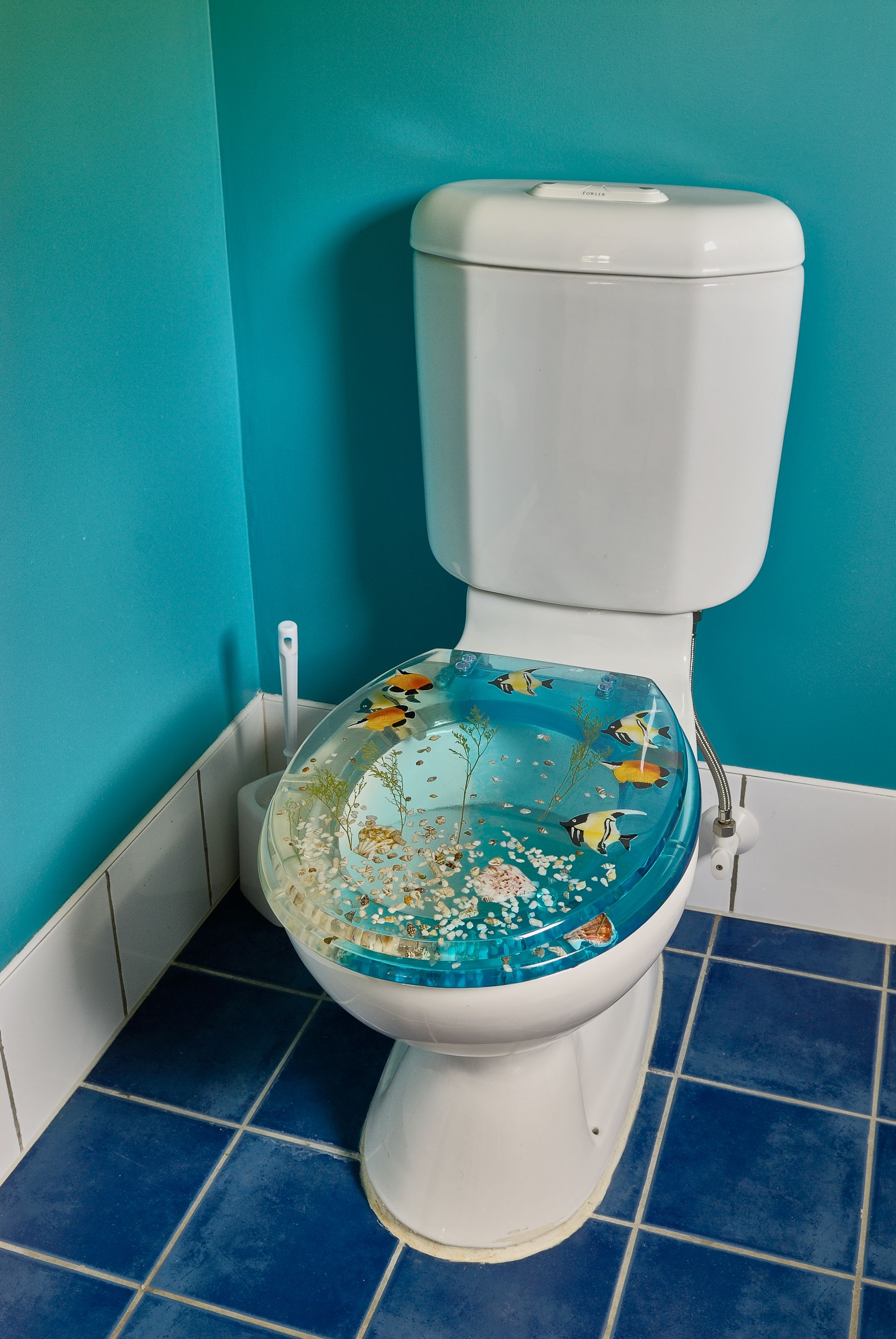 Des toilettes avec un sol carrelé de carreaux bleus et un abattant en verre décoratif.