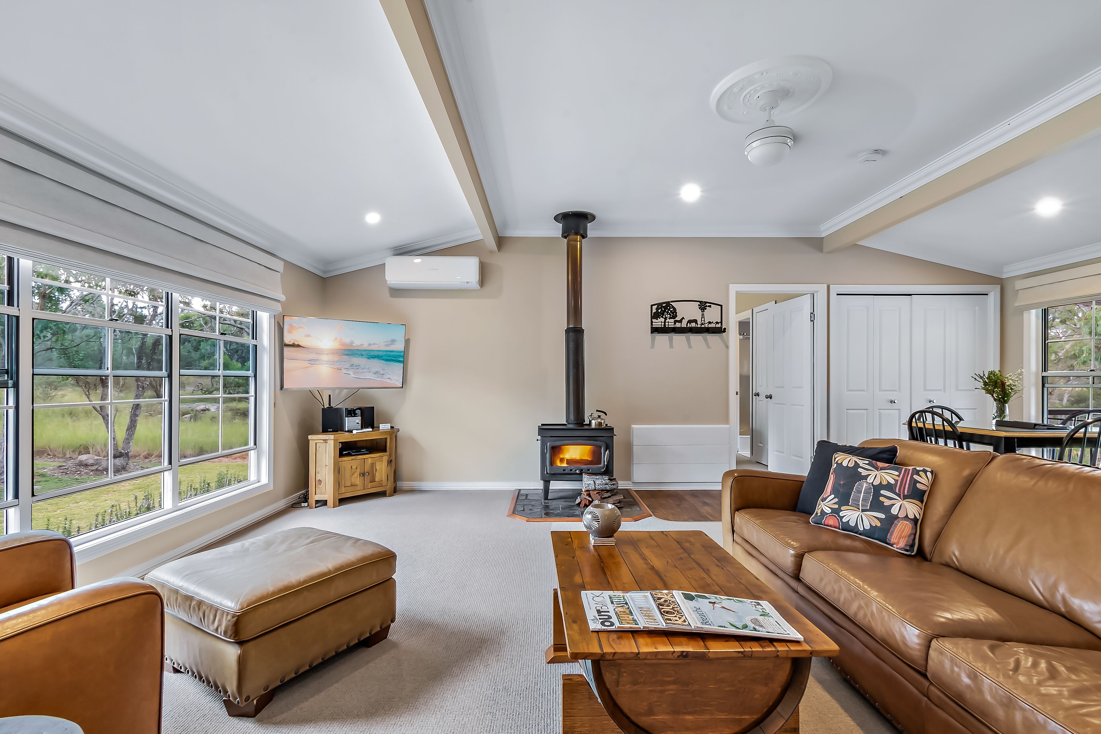 A cozy living room with a fireplace, leather furniture, and large windows offering a view of the outdoors.