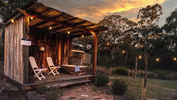 Une cabane en bois rustique dotée d’une véranda, de deux fauteuils et d’une petite table.