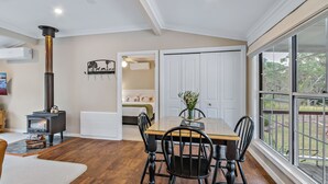 Une pièce avec un poêle à bois, une table à manger avec des chaises, une grande fenêtre et une porte donnant sur une autre pièce.