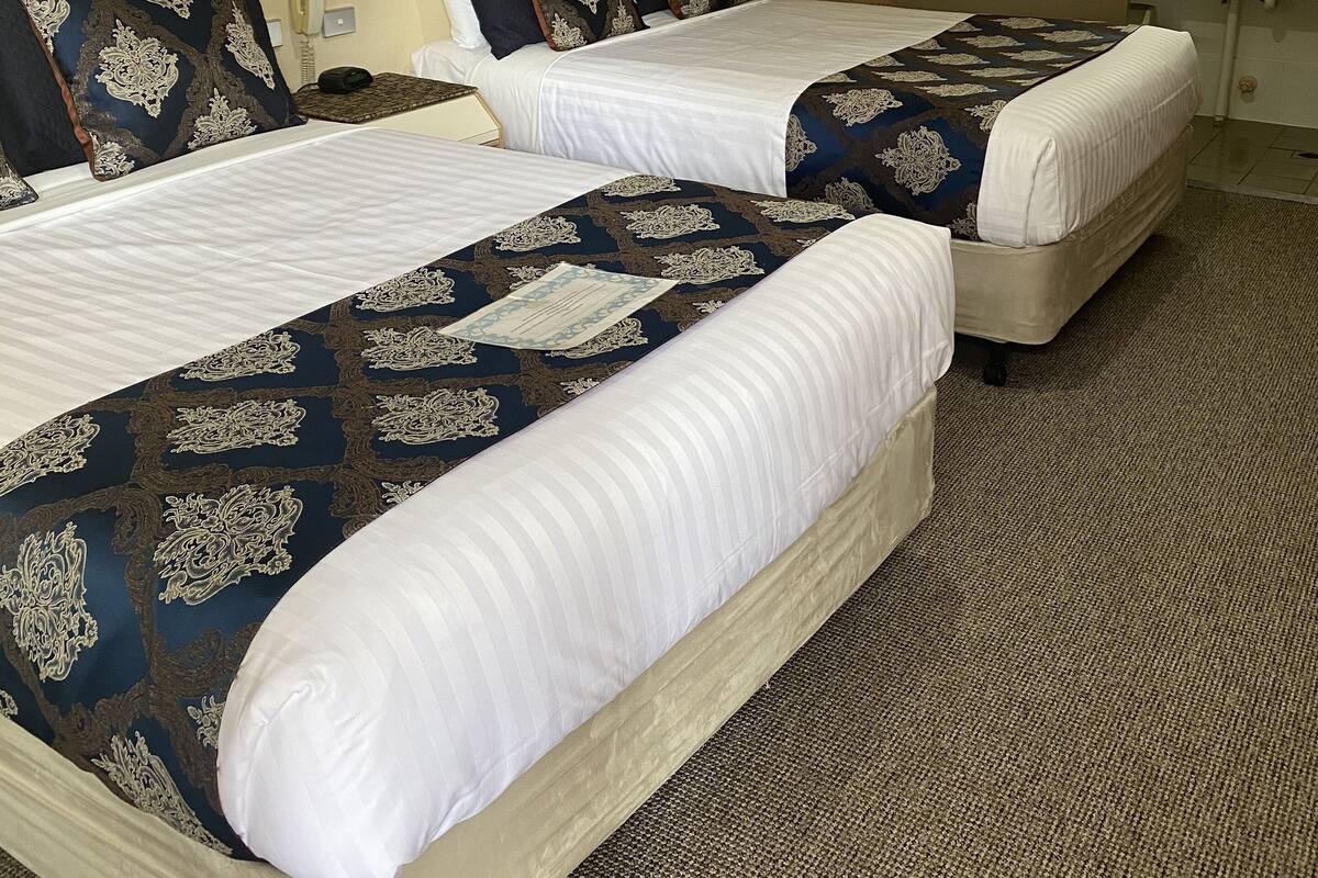Quarto de hotel com duas camas, uma parede de tijolos, banheiro com pia e um objeto decorativo na parede.