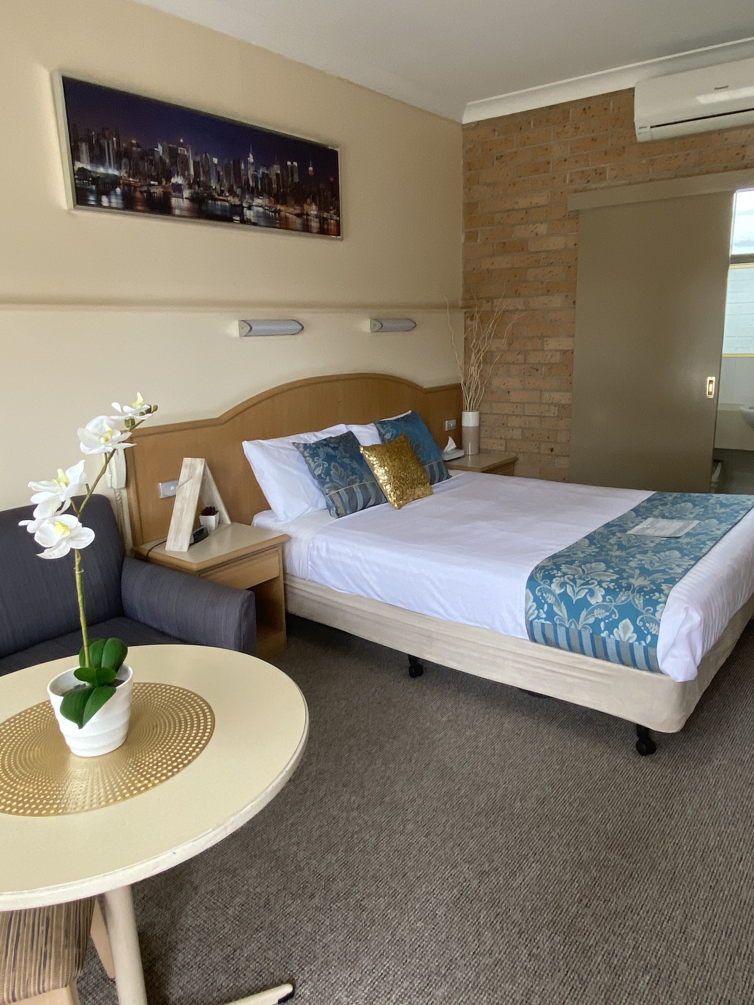 Een hotelkamer met een bed, een nachtkastje, een tafel met een bloevas en een schilderij aan de muur.