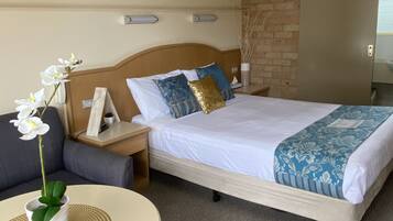 Een hotelkamer met een bed, een nachtkastje, een tafel met een bloevas en een schilderij aan de muur.