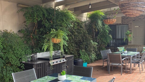 Une terrasse extérieure dotée d’un barbecue, d’une table à manger et de chaises, le tout entouré d’une végétation luxuriante.