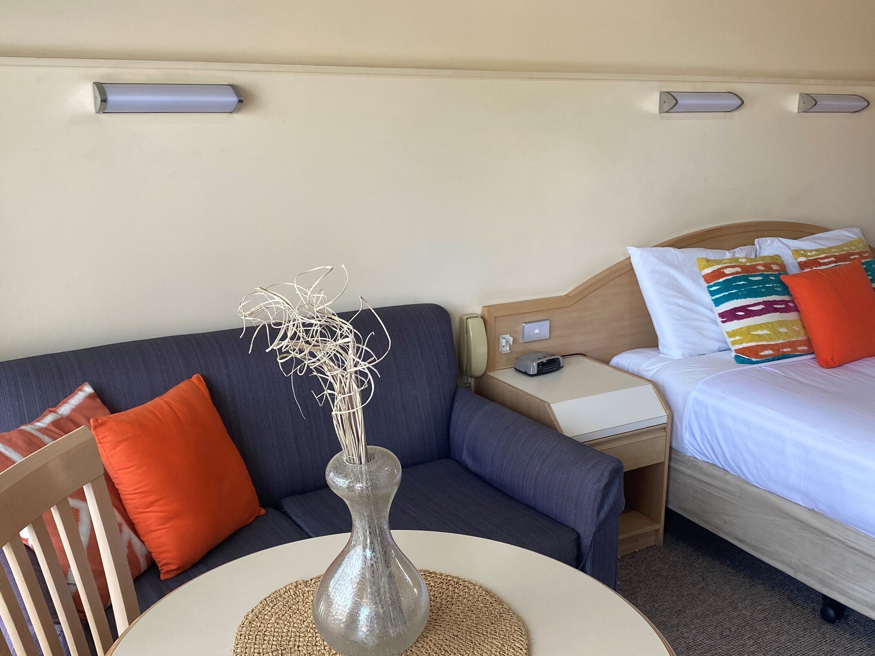 Une chambre d’hôtel avec un lit, une table de chevet, une table ornée d’un vase et un canapé.