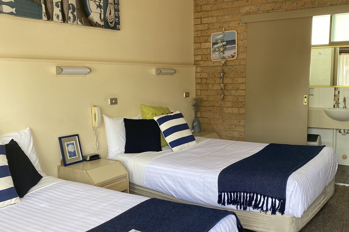 A hotel room with two beds, a brick wall, a bathroom with a sink, and a large mirror.