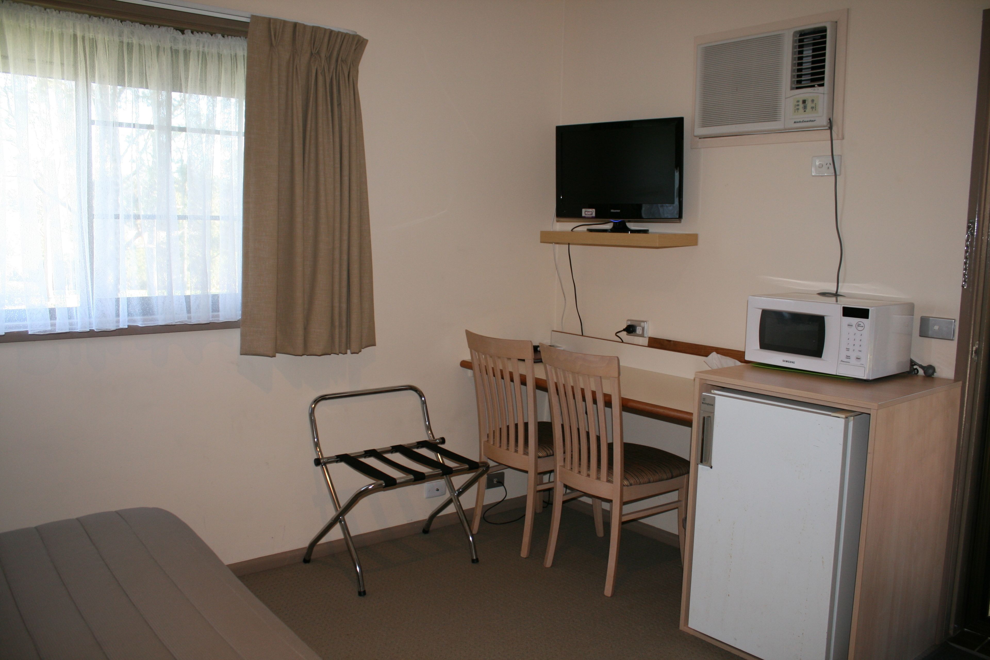 A small room with a bed, a desk with a computer, a chair, a microwave, and a TV.