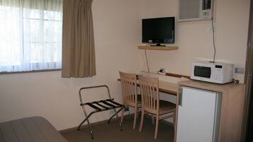 A small room with a bed, a desk with a computer, a chair, a microwave, and a TV.