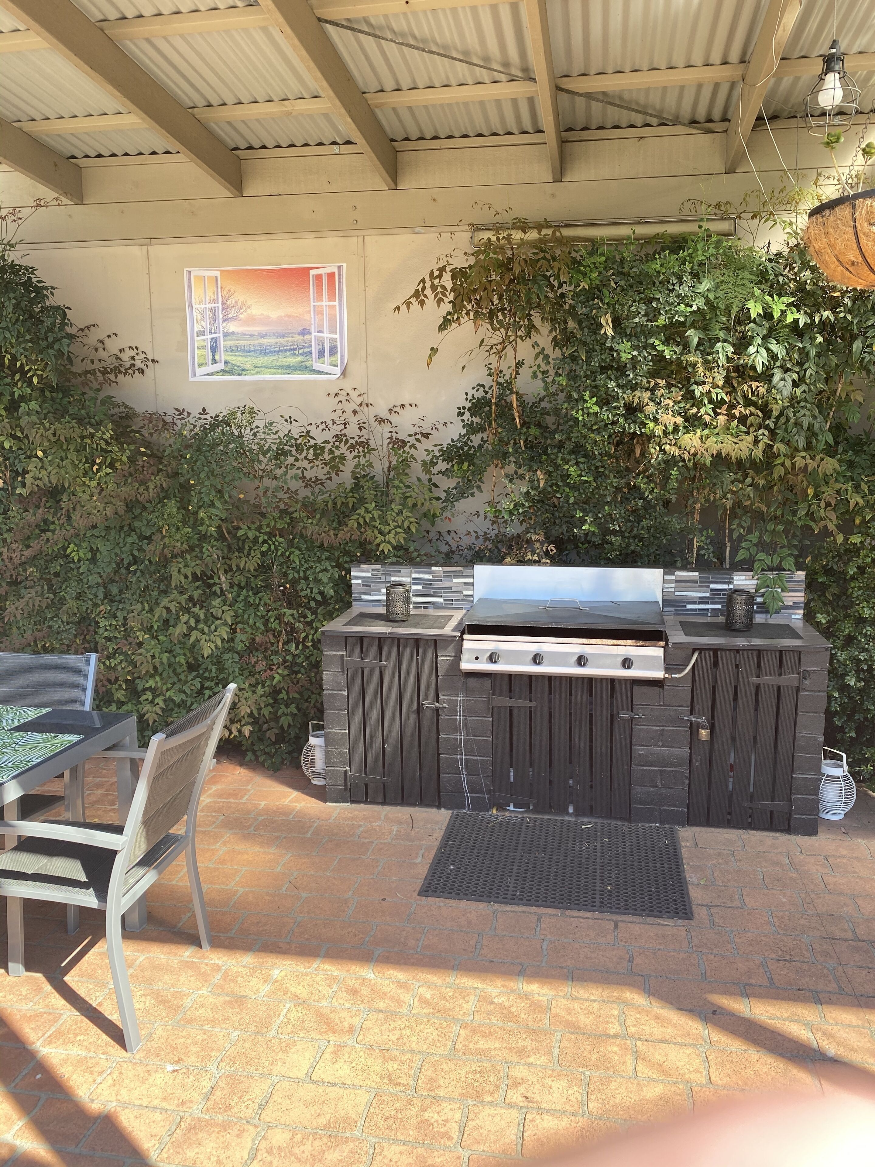 An outdoor patio with a grill, a table with chairs, and a view of the countryside through a window.