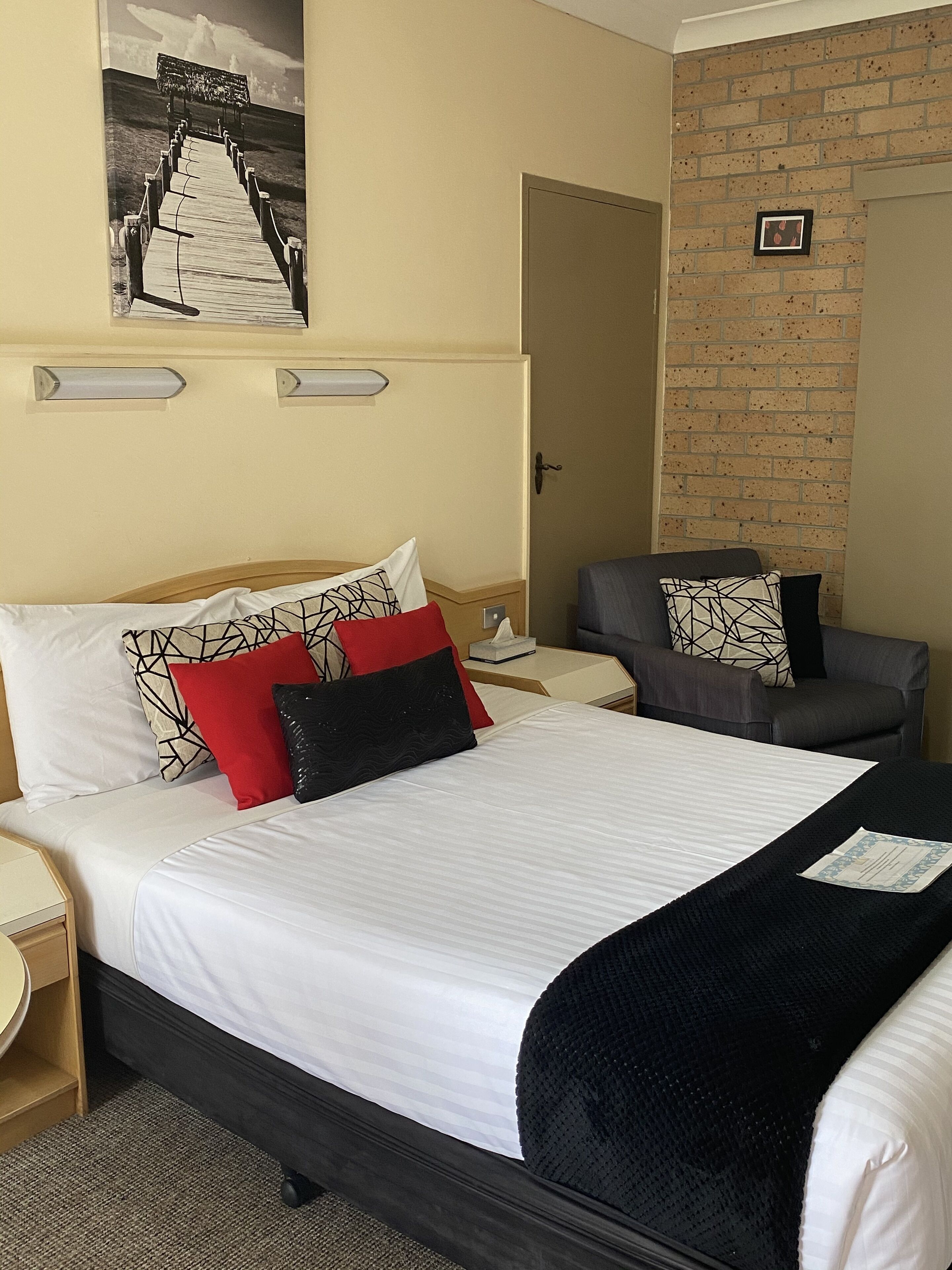 A hotel room with a bed, a chair, a nightstand, and a wall-mounted picture.