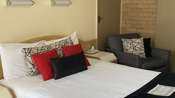 A hotel room with a bed, a chair, a nightstand, and a wall-mounted picture.