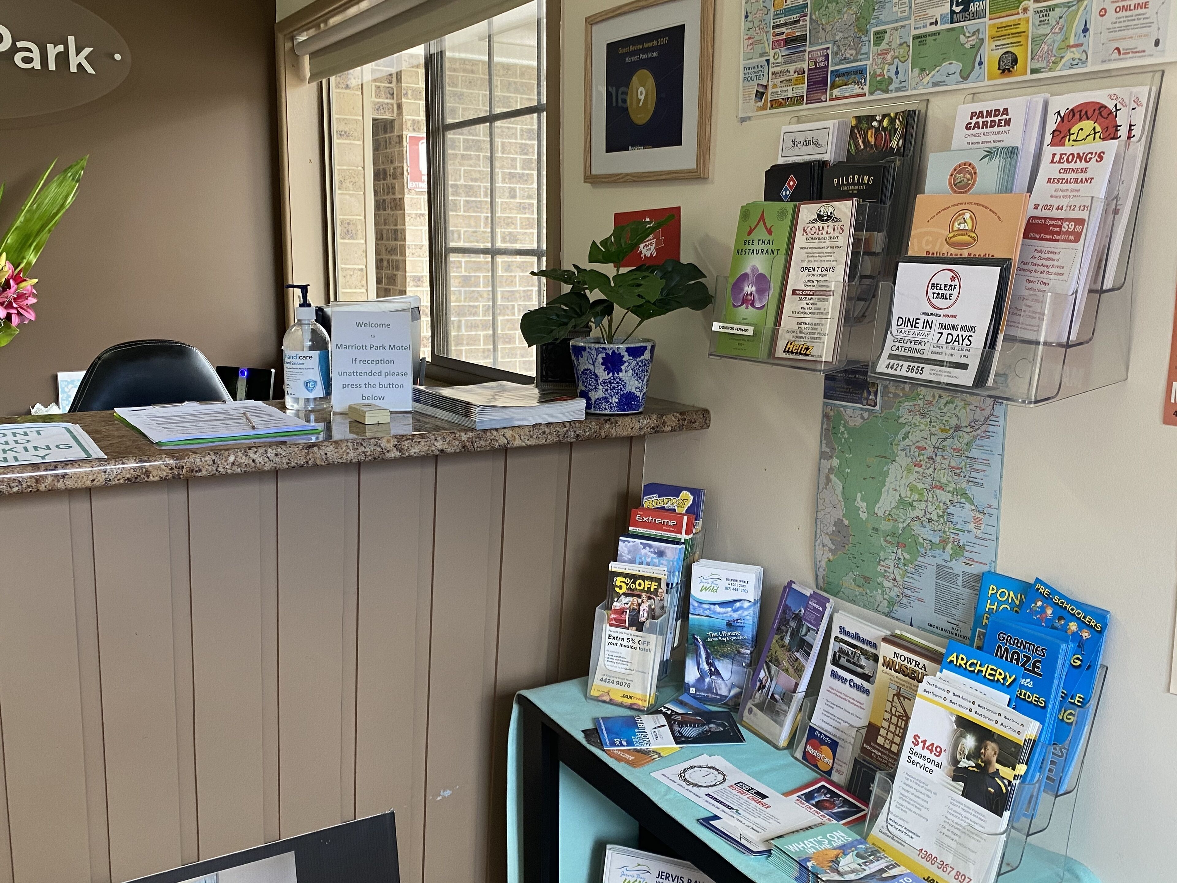 A hotel reception desk with a plant, informational brochures, and a framed award.