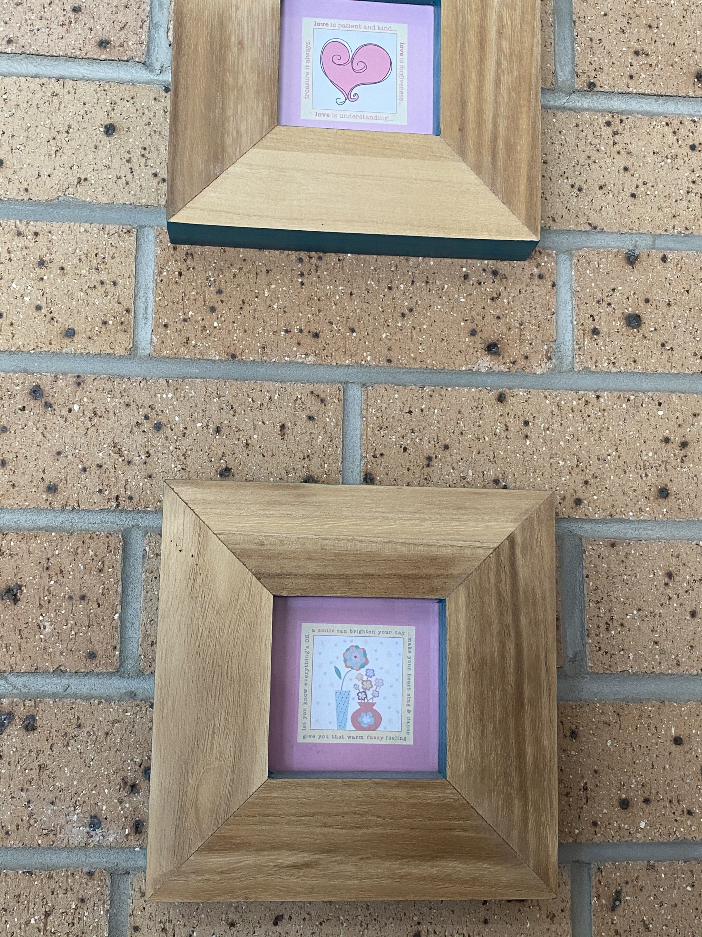 Two wooden picture frames against a brick wall.