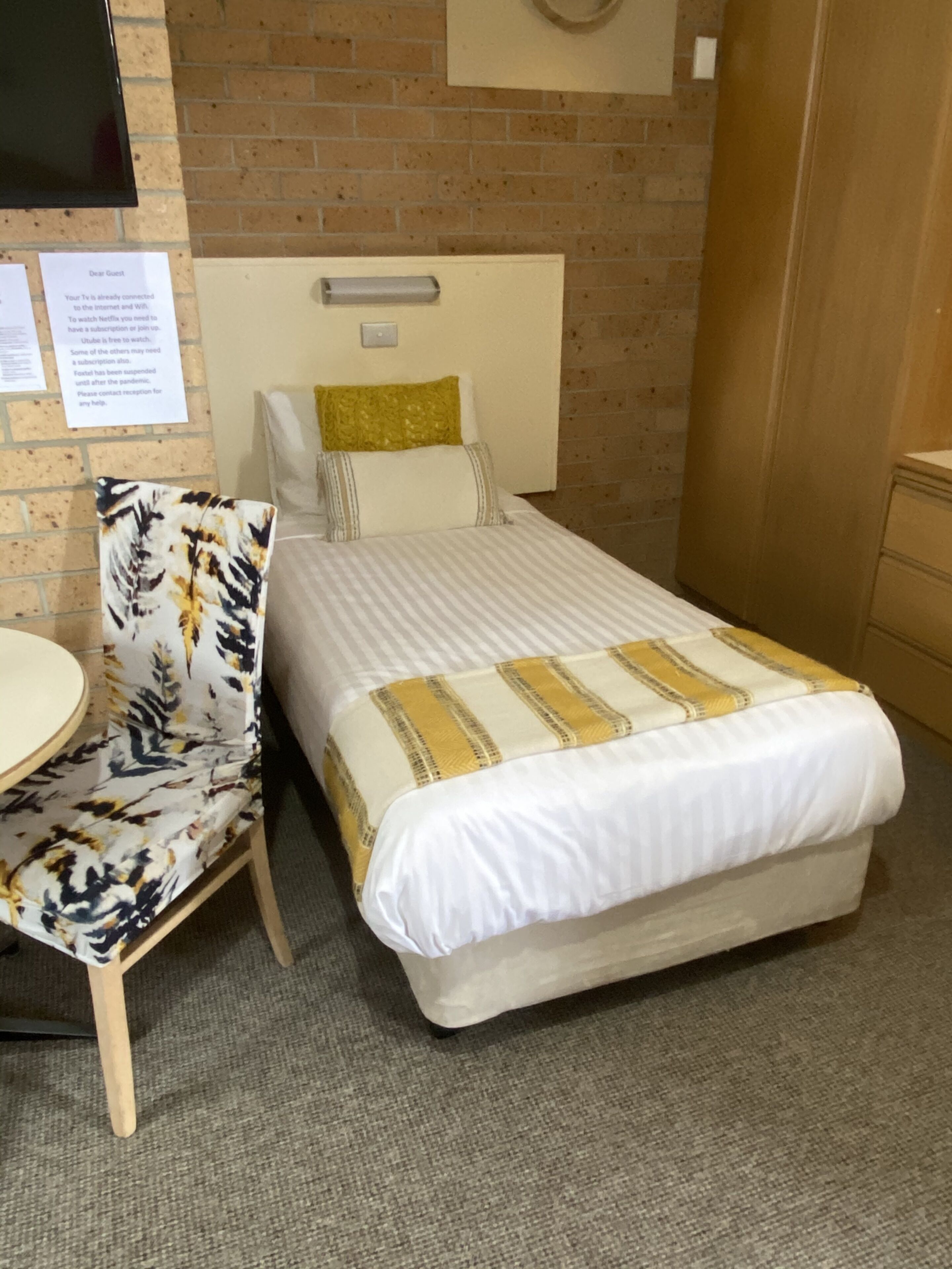 A hotel room with a bed, a chair, a desk, and a TV mounted on the wall.