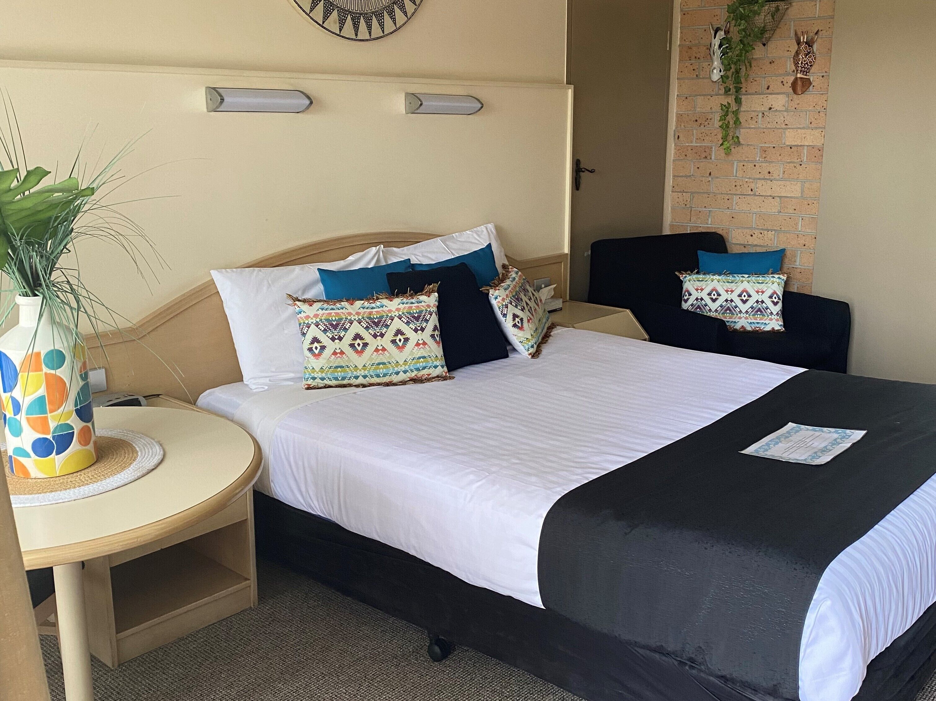 A double bed with white and black bedding, a small bedside table with a vase, and a wall-mounted clock.