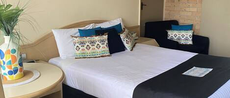 Una cama doble con ropa de cama blanca y negra, una mesita de noche pequeña con un florero, y un reloj de pared.