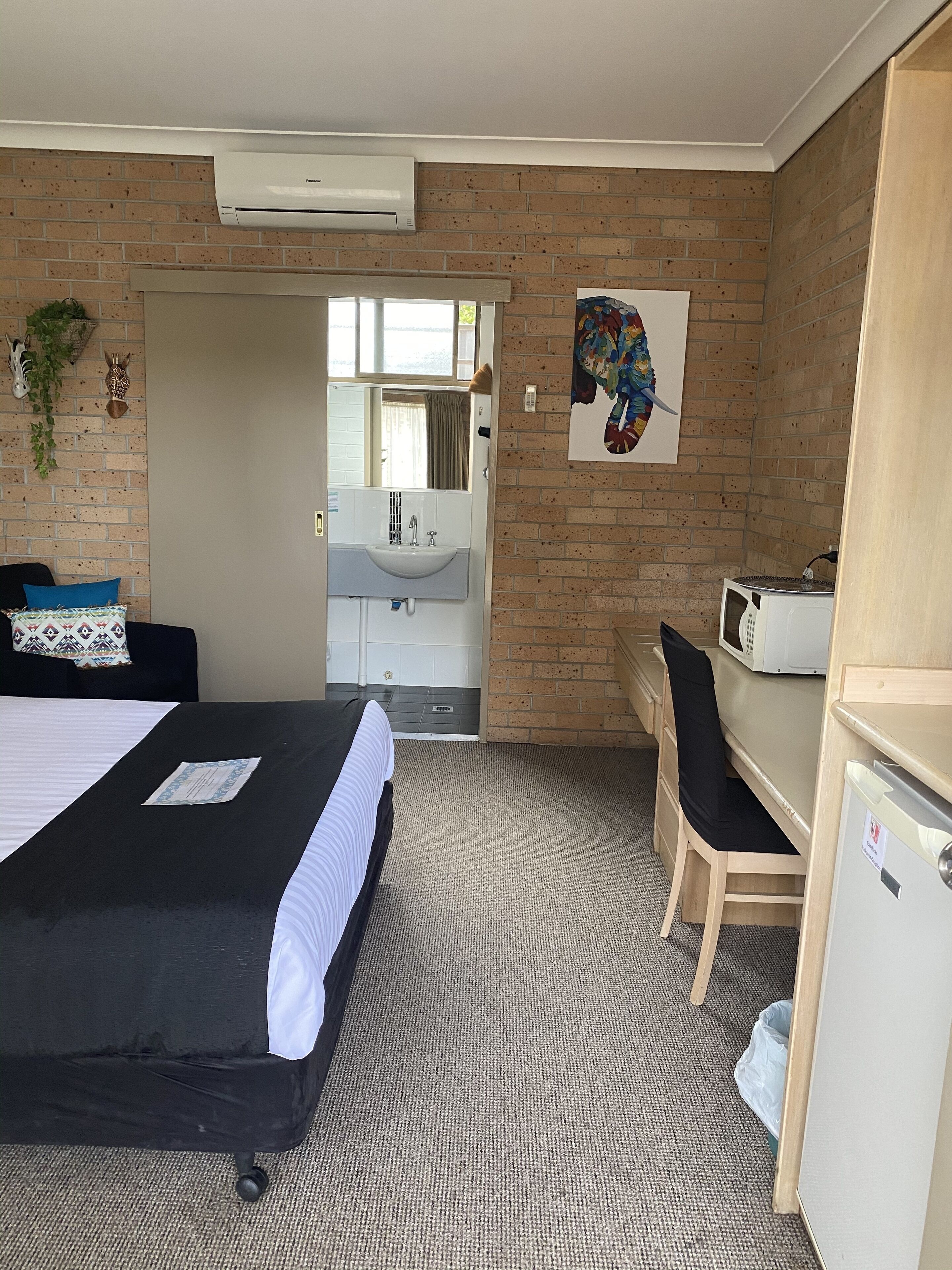 A hotel room with a bed, a desk, a microwave, and a refrigerator.