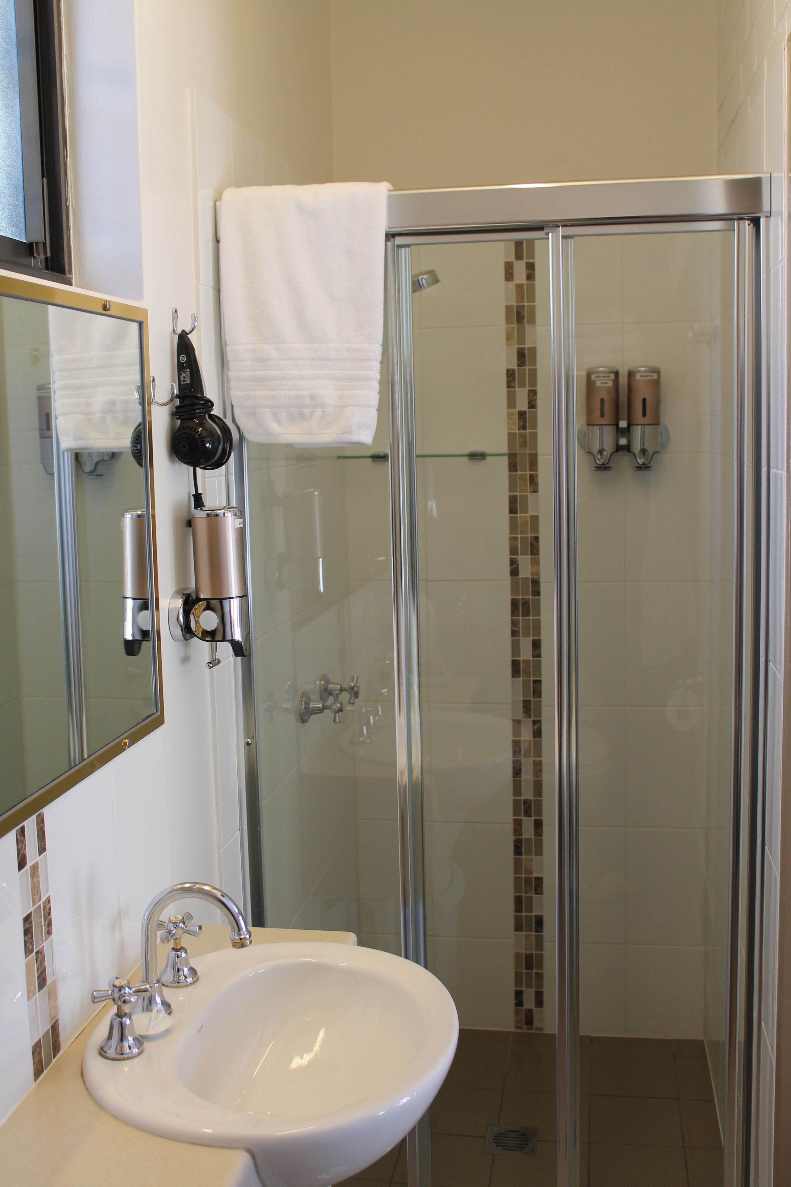 A bathroom with a glass-enclosed shower, a sink with a mirror, and a towel hanging on the wall.