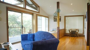 Un salón espacioso con sofá azul, suelo de madera y amplias ventanas con vistas al exterior.