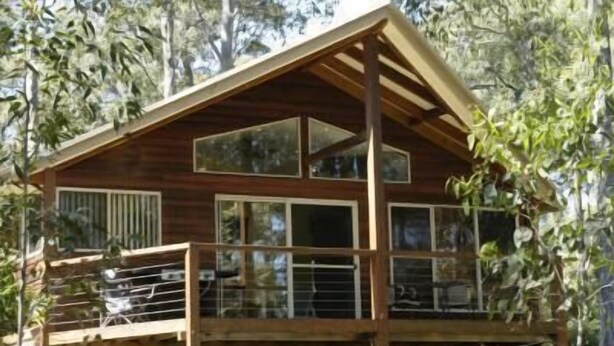 Una cabaña de madera con balcón, ventanas amplias y techo inclinado.