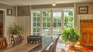 Un comedor con una mesa larga, sillas y plantas en macetas.