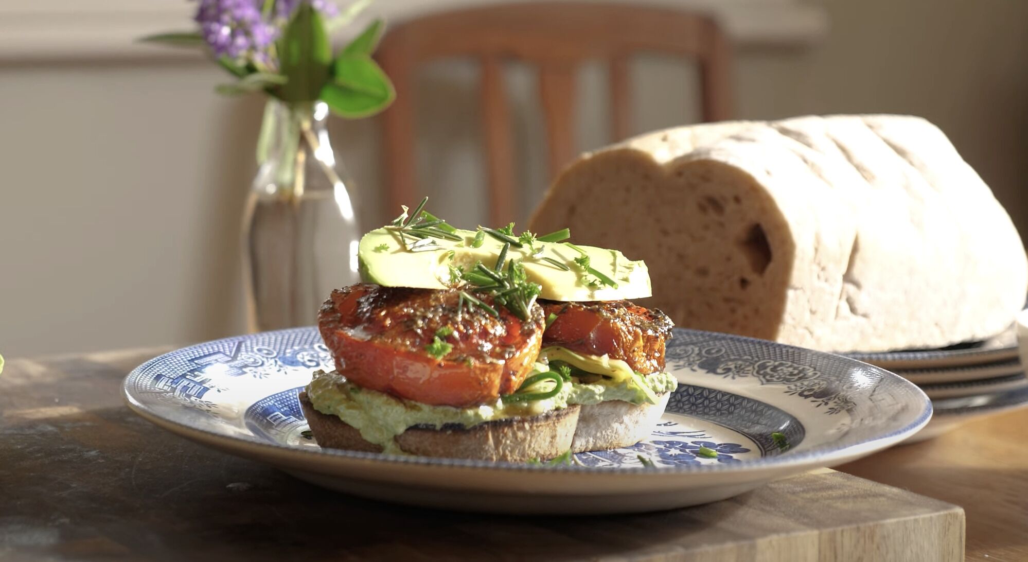 A sandwich on a plate with a loaf of bread in the background.