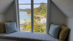 Una habitación con un gran ventanal que da a una zona costera con barcos y vegetación.