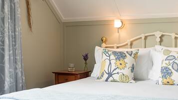 Una cama bien hecha con almohadas florales, una mesita de noche con un vaso y una lámpara de pared.