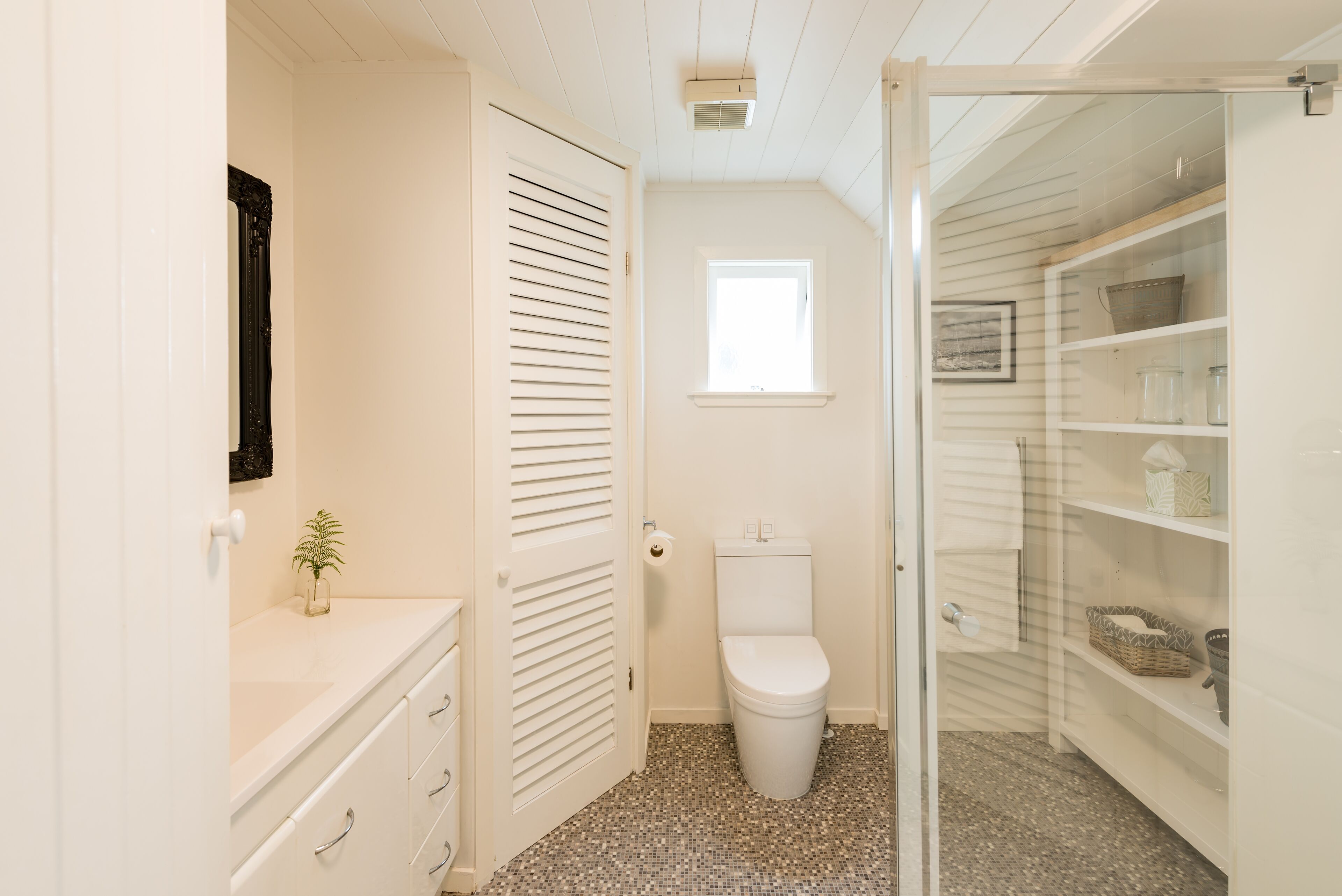 A compact bathroom with a toilet, a small window, and a vanity with drawers.