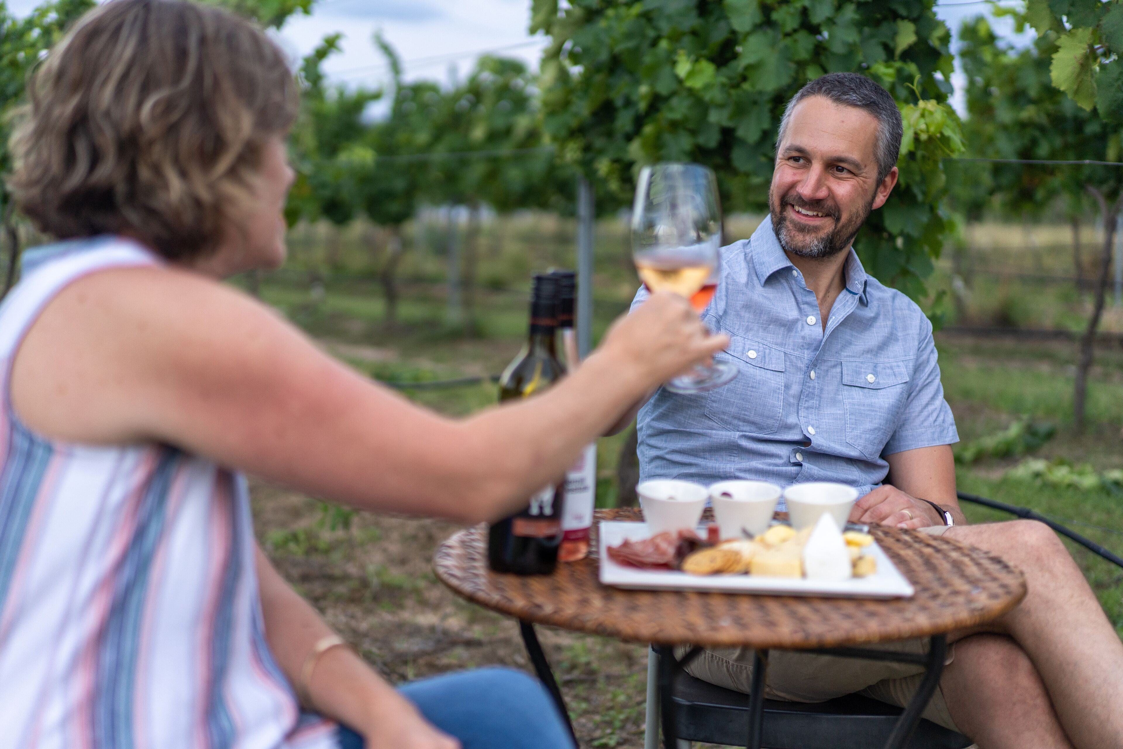 Two people sitting at an outdoor table with a bottle of wine, glasses, and a plate of food.